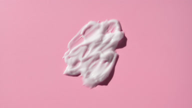 Macro of white cosmetic lotion smears on pale pink background