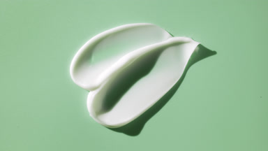Macro crane shot of white eye cream smears on green background