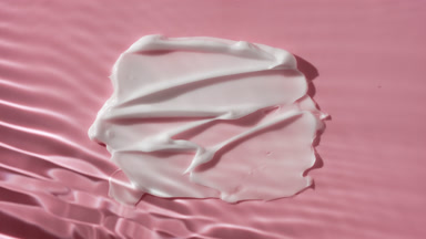 White body cream smears on pink background under rippling water
