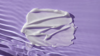 White body cream smears on purple background under water ripples