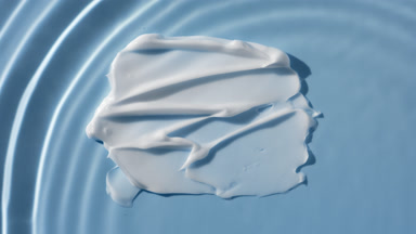 Drop falls down on water on blue background with white cream
