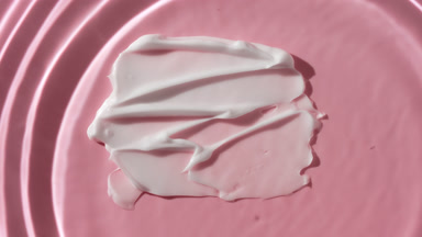 Drop drips on water on pink background with white cosmetic cream