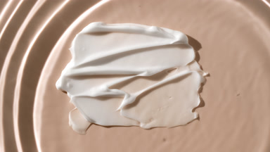 Drop drips on water on beige background with white cosmetic cream