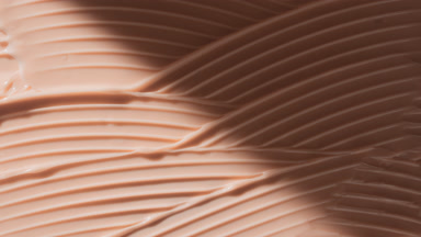 Macro of beige lifting cream wave texture appears from shadow