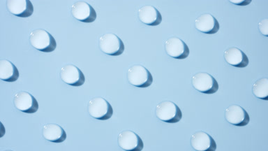Top view of moving transparent drops on pale blue background