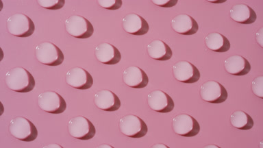 Top view macro of moving transparent drops on pink background