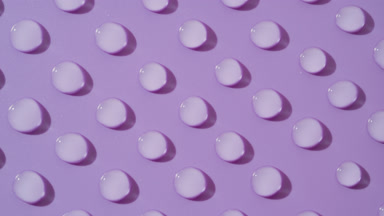 Top view macro of moving transparent drops on violet background
