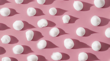 White cream drops on pale pink background with moving lighting