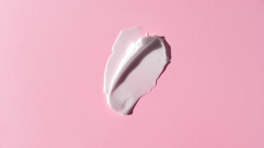 Two white face cream smears on pink background with moving light