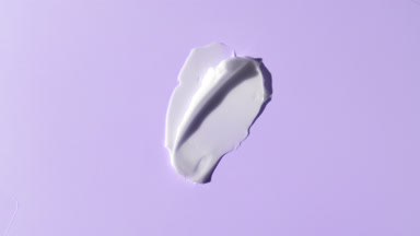White face cream smears on violet background with moving light