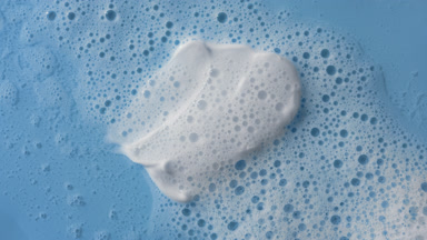 White cream smears on blue background covered by foamy water