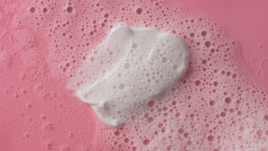 White cream smears on pink background covered by foamy water