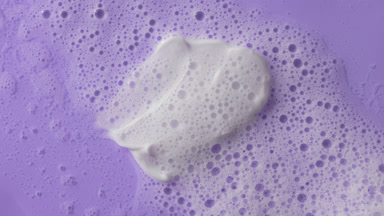 White cream smears on purple background covered by foamy water