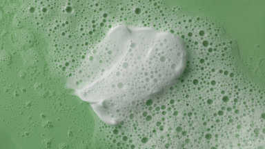 White cream smears on green background covered by foamy water
