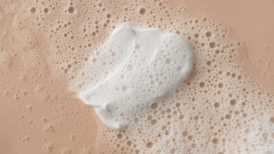 White cream smears on beige background covered by foamy water