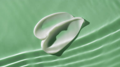 Two white cream smears on green background under rippling water