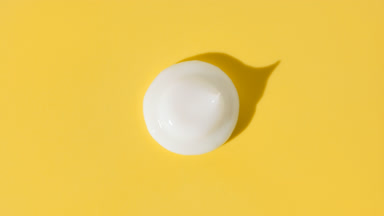 White eye cream drop appears from shadow on yellow background