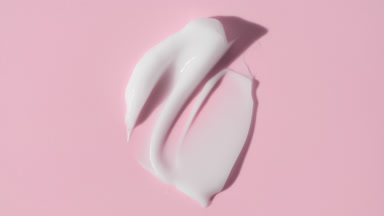 Face cream smears appear from shadow on pale pink background