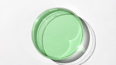 Green eye gel on glass is covered by shadow on white background