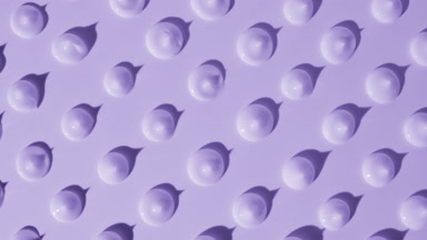Drops of purple cream appear from shadow on purple background