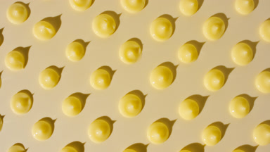 Drops of yellow cream appear from shadow on yellow background
