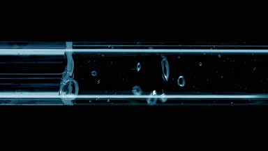 Water is being poured into blue test tube on black background