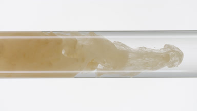 Beige ink filling glass test tube with water on white background