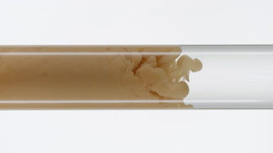 Beige ink flows inside test tube with water on white background