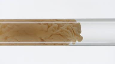Beige ink fills glass test tube with water on white background