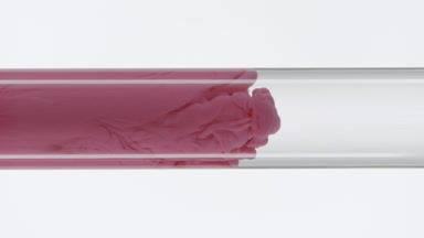Pink ink fills glass test tube with water on white background
