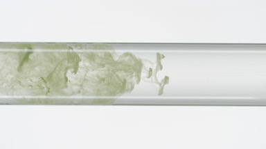 Green ink filling glass test tube with water on white background