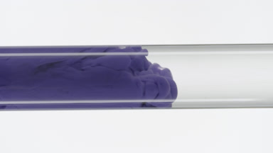 Violet ink fills glass test tube with water on white background