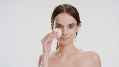 Beautiful Caucasian woman strokes face using cotton pad smiling