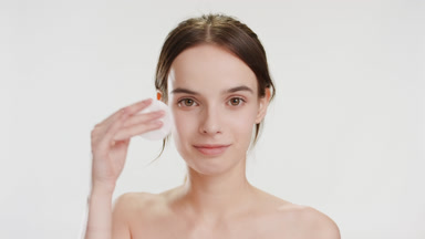 Cute slim Caucasian woman strokes face using cotton pad smiling