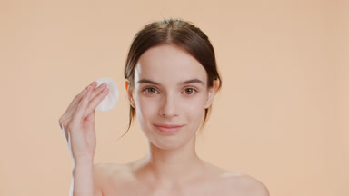Good-looking young woman strokes face using cotton pad smiling