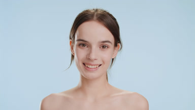 Young woman turns head to camera smiling wide on blue background