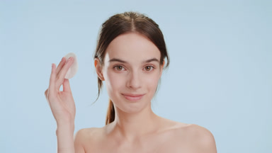 Beautiful slim woman strokes face using cotton pad smiling wide