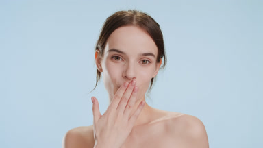 Cute young Caucasian woman blows a kiss on pale blue background