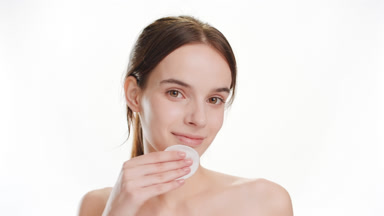 Good-looking woman strokes chin using cotton pad smiling widely