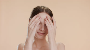 Attractive woman strokes forehead smiling on beige background