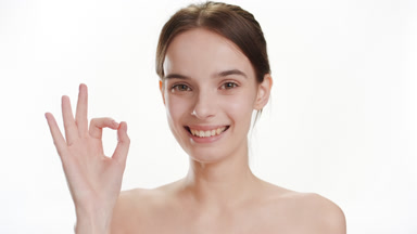 Attractive young slim Caucasian woman shows OK sign smiling wide