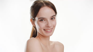 Gorgeous woman strokes shoulder turning body and smiles widely