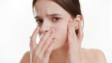 Slim woman touches her cheek stretching skin on white background