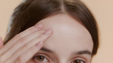 Brown-haired woman strokes her forehead on beige background
