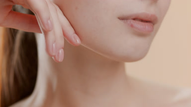 Woman strokes jawline looking aside on beige background
