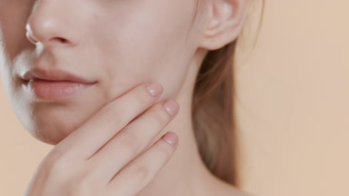 Woman strokes jawline turning head to camera on beige background