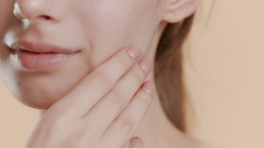 Female model strokes jawline, smiles widely on beige background