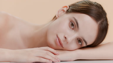 Gorgeous woman puts head on bent arm smiling on beige background