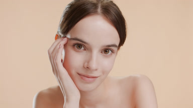 Pretty young woman puts head on hand smiling on beige background