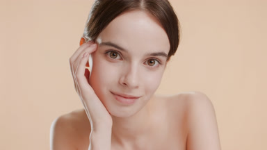 Cute young woman puts head on hand smiling on beige background